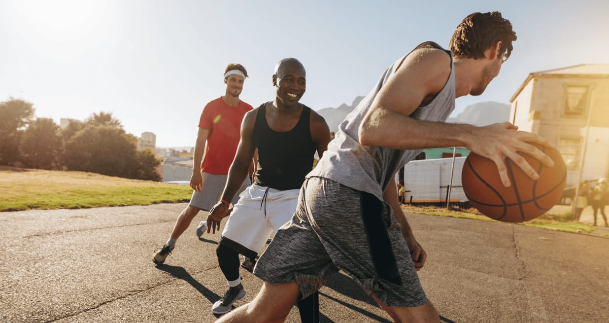 Active men playing basketball outdoors, representing a return to sport after arthroscopic knee surgery recovery at Tyrance Orthopedics in Delray Beach.
