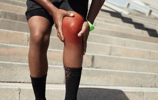 Runner gripping a red, inflamed knee on outdoor stairs, illustrating knee osteoarthritis pain treated with regenerative options at Tyrance Orthopedics in Delray Beach.