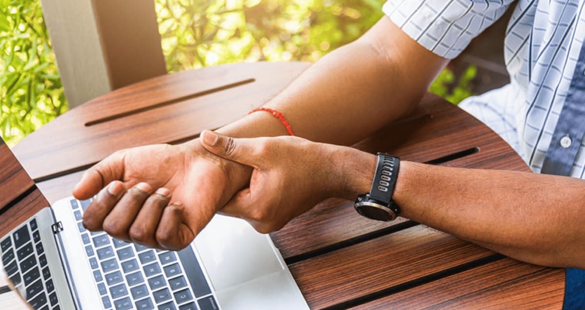 Person at a laptop gripping a painful wrist, a common sign of carpal tunnel syndrome treated with in-office WALANT release at Tyrance Orthopedics in Delray Beach.