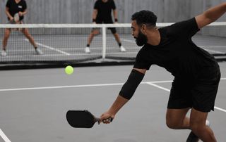 Pickleball player lunging to return the ball with a paddle during a match while wearing an elbow sleeve, illustrating common pickleball injuries seen at Tyrance Orthopedics in Palm Beach.
