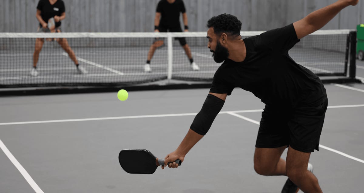 Pickleball player lunging to return the ball with a paddle during a match while wearing an elbow sleeve, illustrating common pickleball injuries seen at Tyrance Orthopedics in Palm Beach.