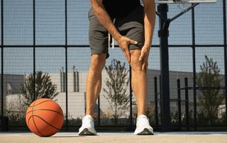 Basketball player on an outdoor court gripping his knee in pain, a common sign of a meniscus tear treated without surgery at Tyrance Orthopedics in Palm Beach.