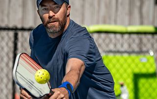 Pickleball player reaching to return the ball with a paddle, using the overhead shoulder motion linked to rotator cuff injuries treated at Tyrance Orthopedics in Palm Beach.