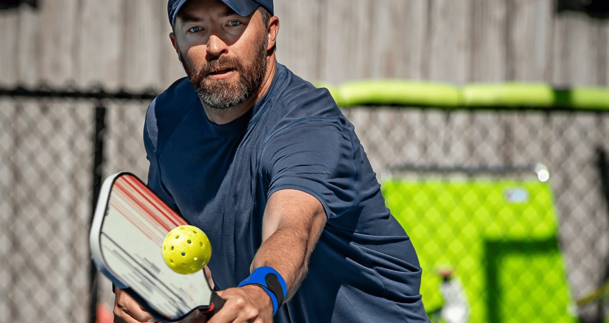 Pickleball player reaching to return the ball with a paddle, using the overhead shoulder motion linked to rotator cuff injuries treated at Tyrance Orthopedics in Palm Beach.