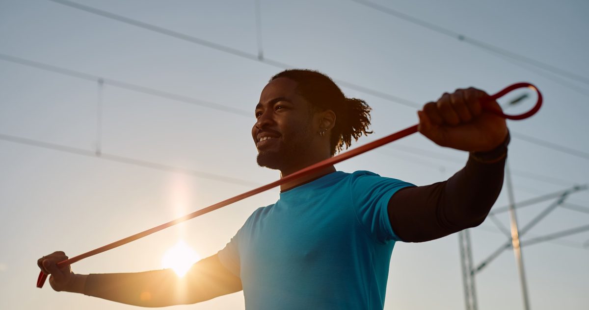 Athlete drawing a resistance band across the shoulders outdoors, the kind of controlled loading that keeps an arthritic AC joint working.