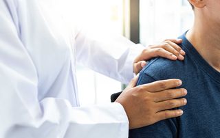 Person pointing to pain on top of the shoulder at the AC joint during an arthritis evaluation.