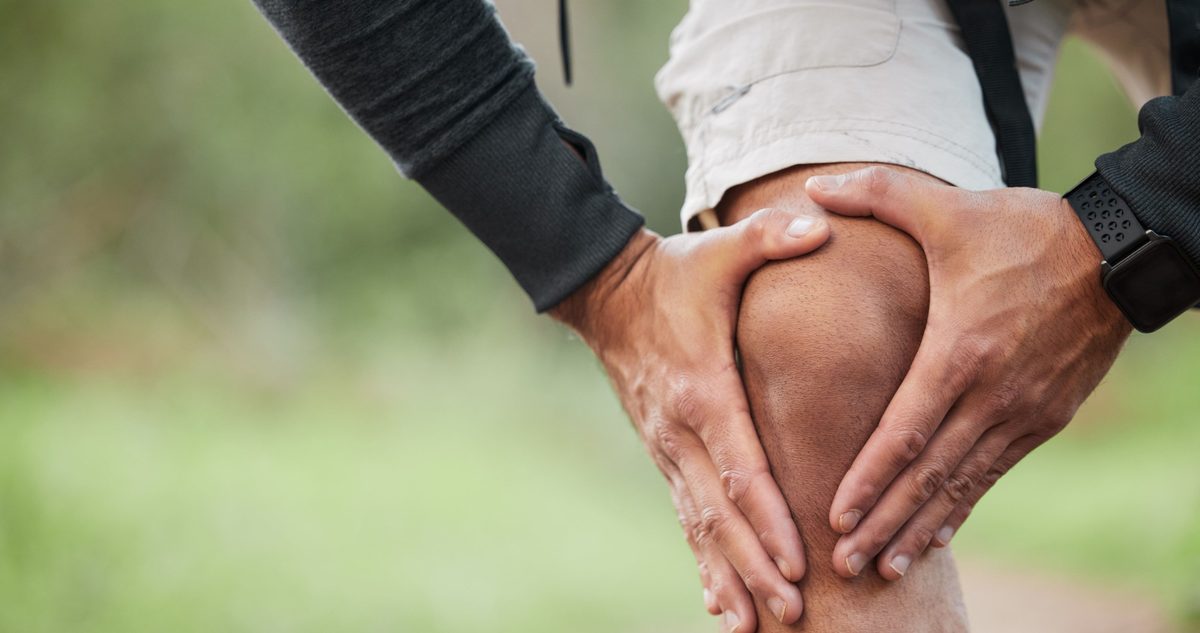 Hiker gripping a painful knee on a trail, the kind of injury that leads to ACL reconstruction and the recovery that follows.