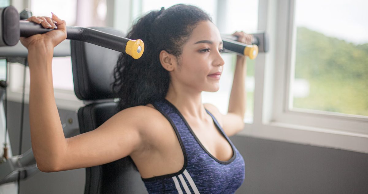 Woman working a shoulder press machine in a gym, the overhead strength PRP treatment is meant to give back.