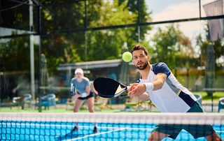 Padel player reaching for a volley at the net, the kind of repeated load that brings players to a sports medicine clinic.
